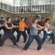 Un grupo de personas practican artes marciales en un espacio cubierto al aire libre. Están de pie en posturas similares con las manos extendidas hacia adelante.