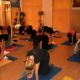 Un grupo de personas participan en una sesión de yoga sobre colchonetas en una habitación poco iluminada, realizando ejercicios sobre manos y rodillas.