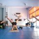 Un grupo de personas practican yoga en un estudio luminoso, acostados boca arriba con las piernas extendidas hacia arriba en forma de V.